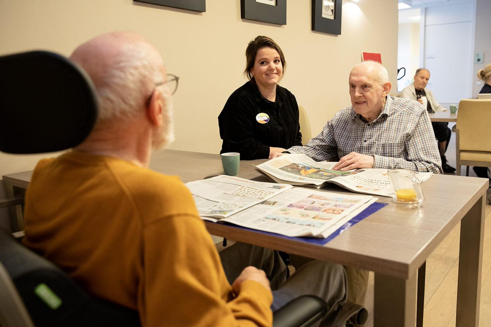 Bewoners en medewerker lezen krant op afdeling Gerontopsychiatrie: Zorg voor ouderen met langdurige psychiatrische problemen